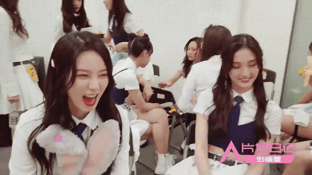 a group of girls are sitting in a room with a pink a on the bottom right