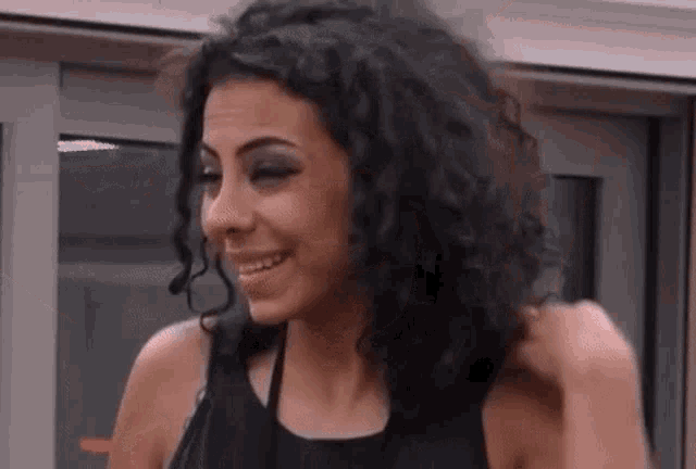 a woman with curly hair wearing a black tank top is smiling .