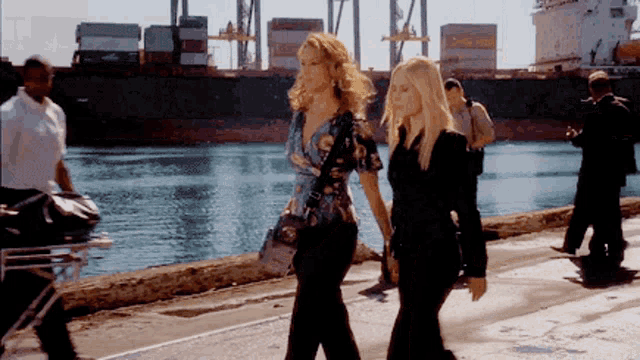 two women walking in front of a large container ship