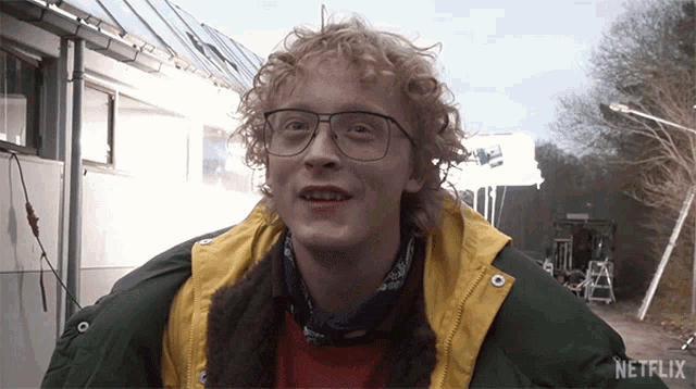 a young man wearing glasses and a yellow jacket has a netflix logo on the bottom of his jacket