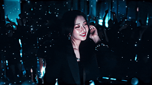 a woman in a black jacket smiles in front of a crowd of people