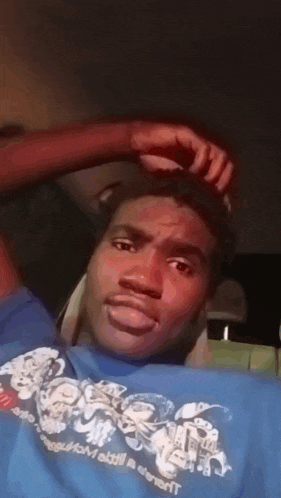 a man wearing a blue shirt that says ' everybody ' on it scratches his head