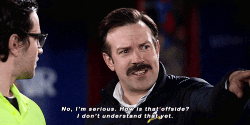 a man with a mustache is talking to another man while wearing glasses and a black jacket .