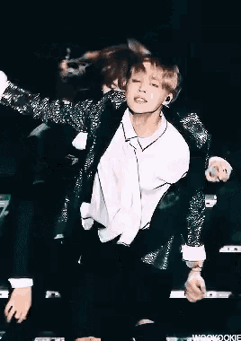 a young man is dancing on a stage in a green jacket and tie .