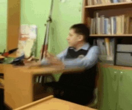 a blurry image of a man sitting at a desk in front of a bookshelf