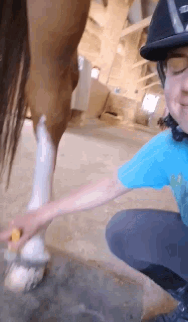 a person wearing a helmet and a blue shirt is kneeling down next to a horse
