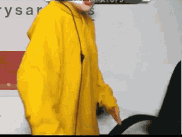 a person wearing a yellow hoodie is standing in front of a sign that says " ysar "