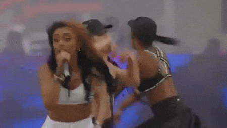 a group of women are dancing on a stage in front of a large purple sign that says ' a ' on it