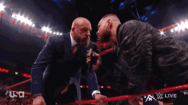 a man in a suit and tie is standing next to another man in a wrestling ring