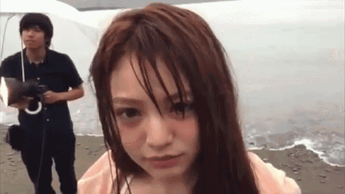 a woman with wet hair looks at the camera while a man holds an umbrella behind her