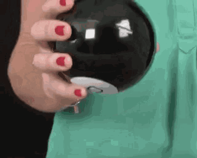 a woman is holding a black ball with red nails .