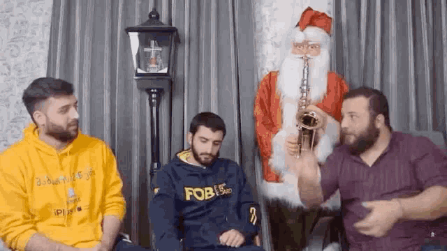a man is playing a saxophone in front of a santa claus statue while three men sit in front of him .
