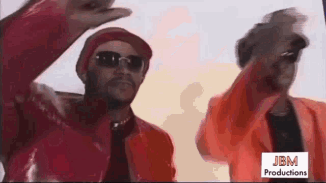 two men wearing red jackets and hats are dancing in front of a sign that says jbm productions .