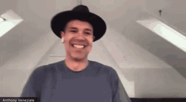 a man wearing a hat and ear buds is smiling while talking on a video call .
