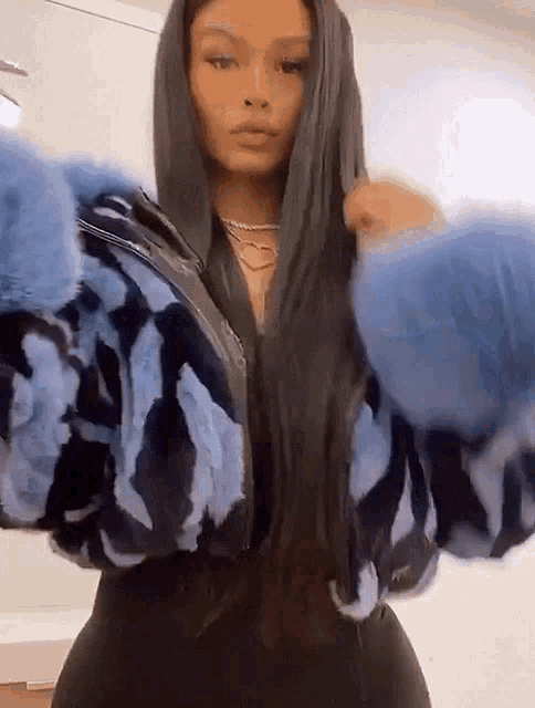 a woman with long black hair is wearing a blue fur jacket and black pants .