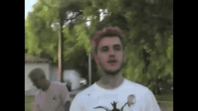 a man with pink hair and a beard is standing in front of a tree .