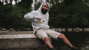 a man in a hoodie sits on a dock near a lake