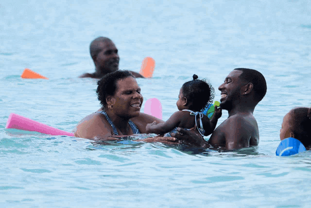 a group of people are playing in the water and one of them is wearing a pink arm float