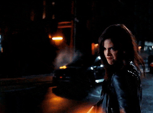 a woman in a black jacket is walking down a dark street
