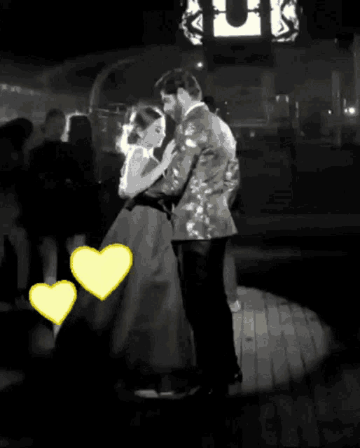 a black and white photo of a man and woman dancing with yellow hearts in the background