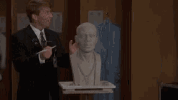 two men in suits are standing next to a statue of a man 's head .