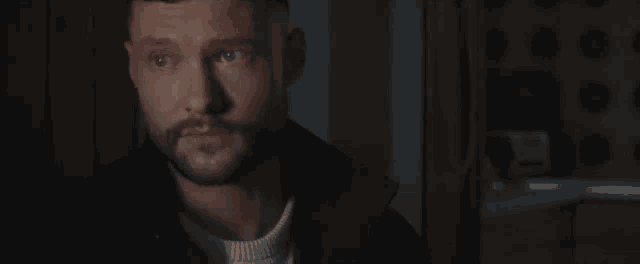 a man with a beard is standing in a dark room looking at something .