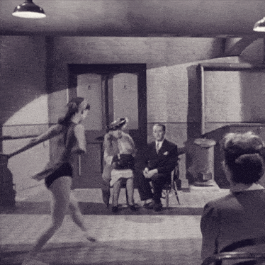 a black and white photo of a woman dancing in front of a man and two women