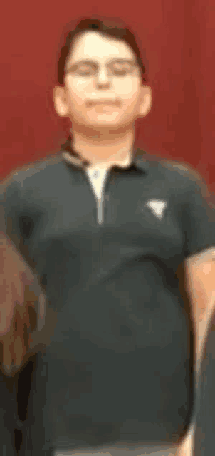 a man wearing glasses and a black shirt is standing in front of a red background .