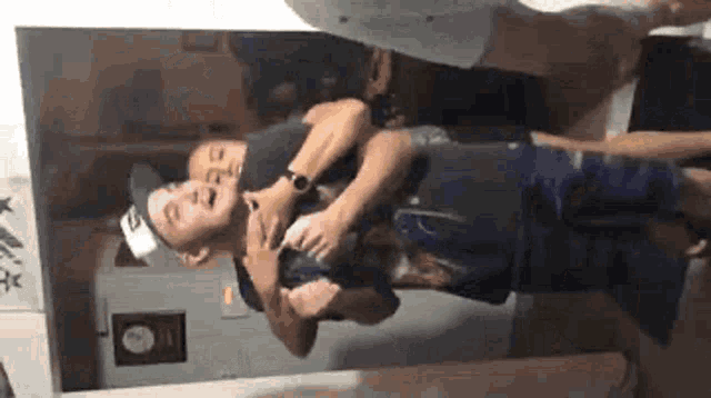 a man in a hat is being held by another man in a room .
