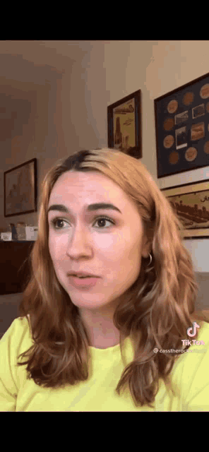 a woman in a yellow shirt is looking at the camera in front of framed pictures