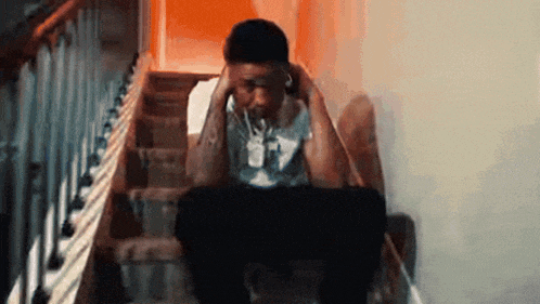 a man is sitting on a set of stairs holding his head .