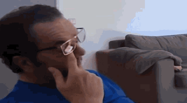 a man wearing glasses is sitting on a couch and touching his face