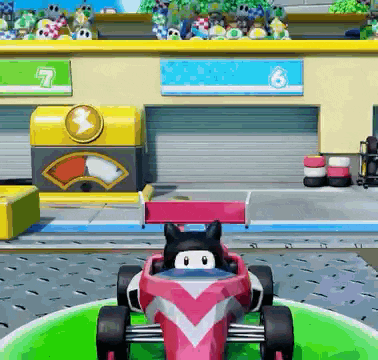 a pink race car with a black cat in the driver 's seat is in front of a building with the number 7 on it