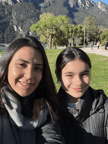 a woman and a girl are posing for a picture in front of mountains