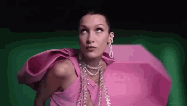 a woman in a pink dress and pearls is standing in front of a green background .