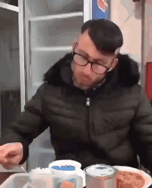 a man wearing glasses is sitting at a table with a plate of food and a can of pepsi
