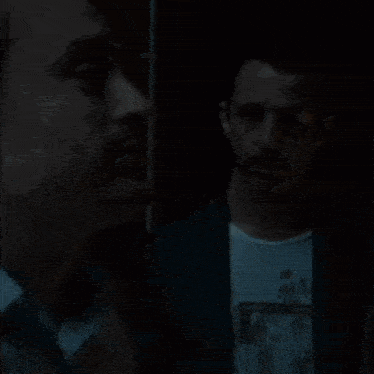 a man in a white shirt is looking at something in the dark