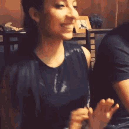 a woman in a black tank top is clapping her hands while sitting at a table in a restaurant .
