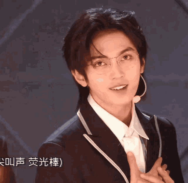 a man wearing glasses and a suit has chinese writing on the bottom right
