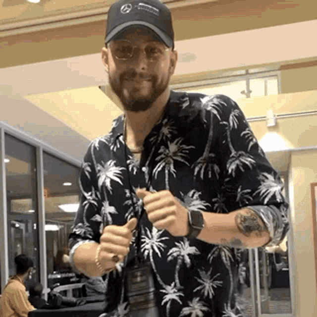 a man wearing a hat and a shirt with palm trees on it is giving a thumbs up