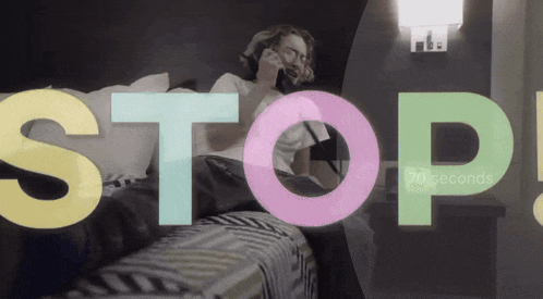 a man is laying on a bed talking on a cell phone and the words stop are behind him