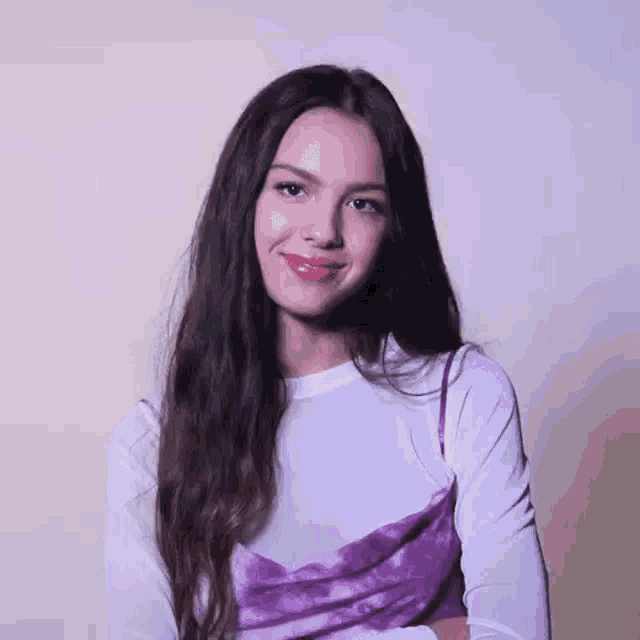 a woman with long hair is wearing a white shirt and a purple dress and smiling .