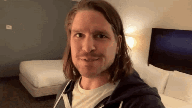 a man with long hair and a beard is standing in a hotel room