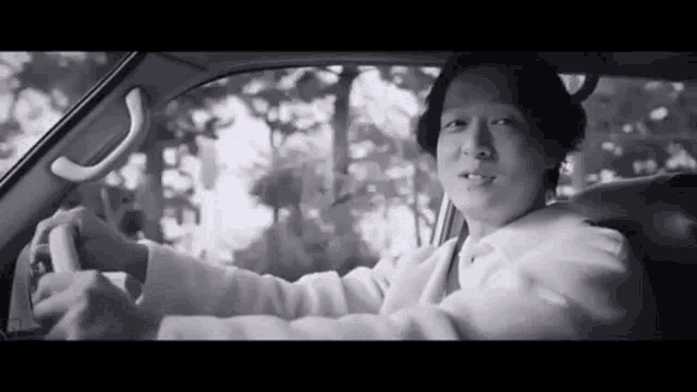 a man in a white suit is driving a car .