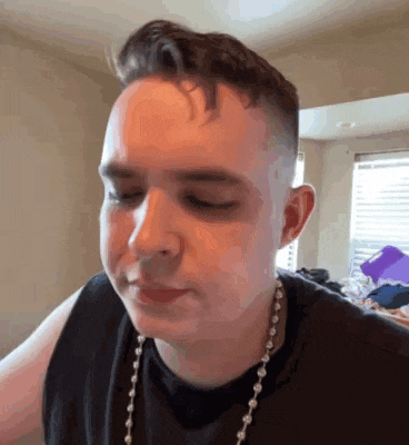 a young man wearing a black tank top and a pearl necklace is making a face .