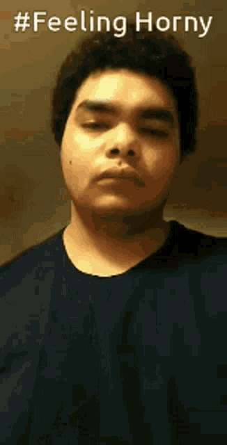 a man in a blue shirt is making a funny face with the words `` feeling horny '' behind him .