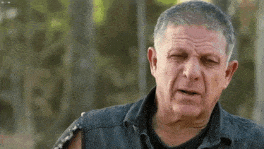 a man with gray hair is wearing a black vest and a black shirt .