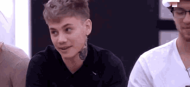 a young man with a tattoo on his neck is sitting at a table with a group of people .