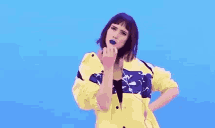 a woman in a yellow jacket is dancing with a donut in her mouth .