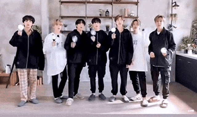 a group of young men are standing next to each other in a room holding lightsticks in their hands .